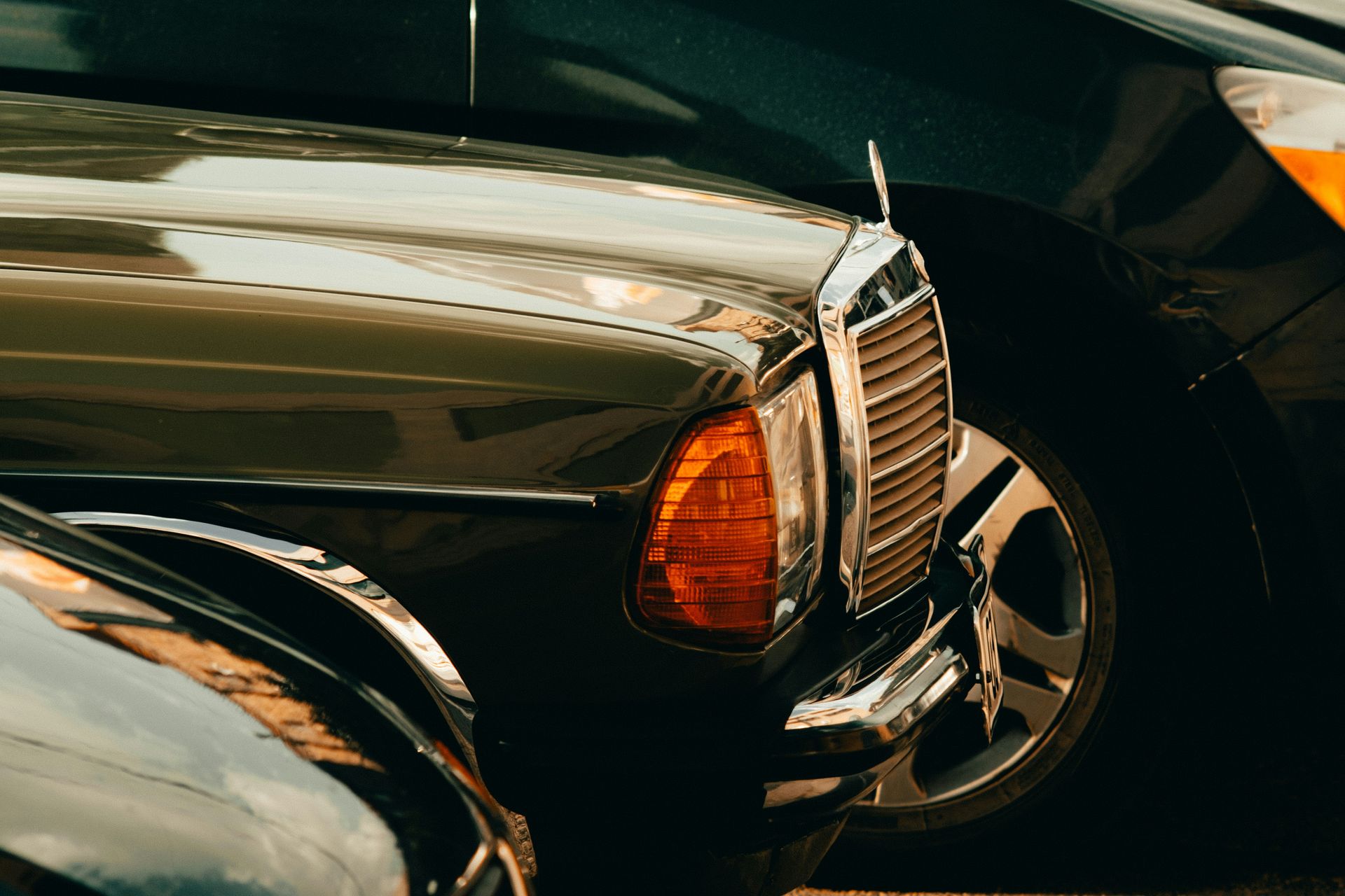 Nahaufnahme der Front eines klassischen dunklen Autos mit orangefarbenem Seitenlicht und Chromgrill.