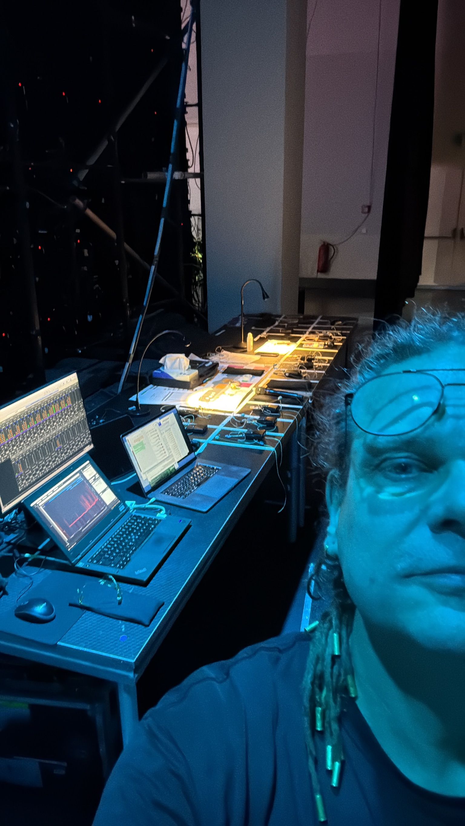 Ein Mann macht ein Selfie an einem Techniktisch, umgeben von Bildschirmen und Geräten. Blaues Licht umspielt die Szene.