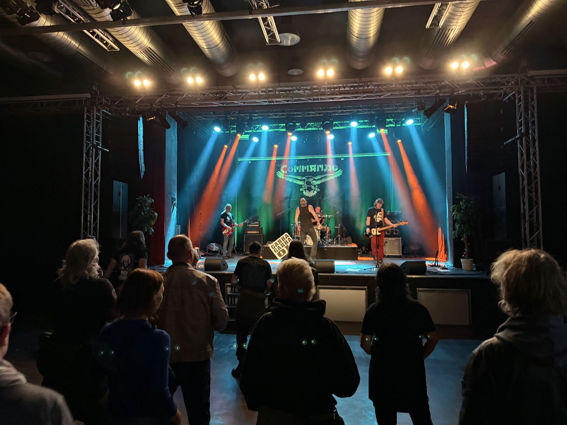 Die Band tritt auf der Bühne mit Bühnenbeleuchtung auf; das Publikum schaut zu.