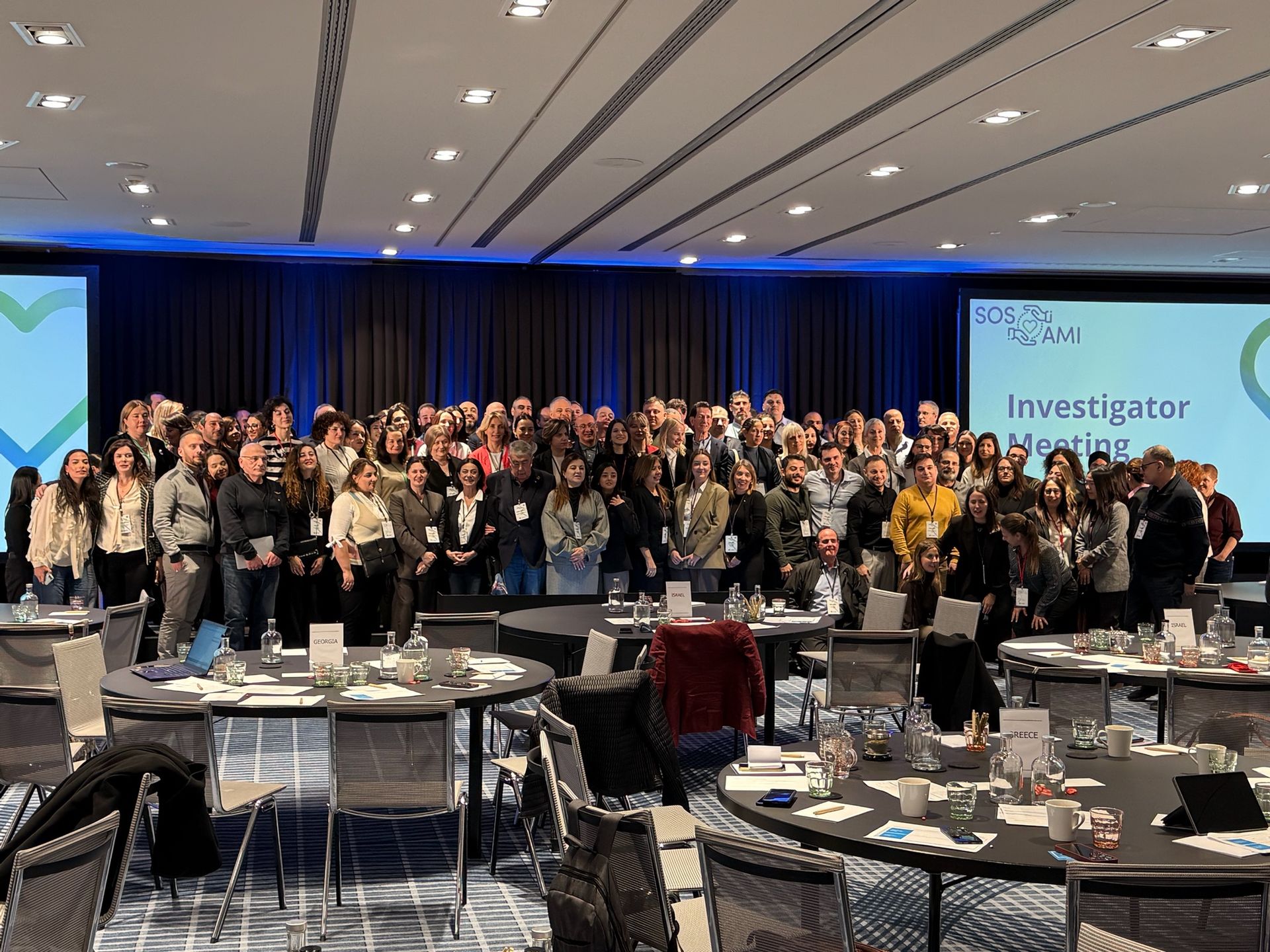 Eine große Gruppe von Menschen posiert in einem Konferenzraum für ein Foto. Tische und Stühle sind im Vordergrund zu sehen.