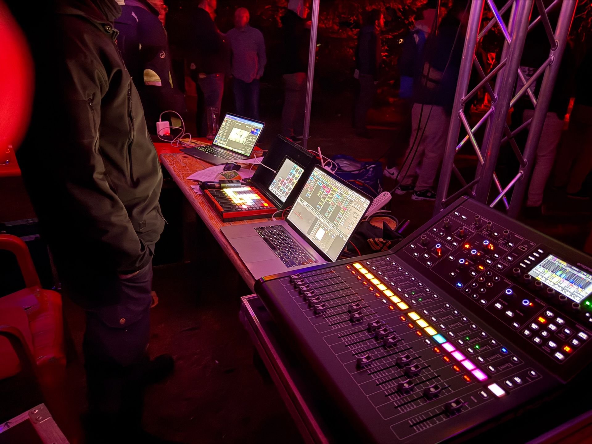 Ein Toningenieur bedient nachts im Freien ein Mischpult; im Hintergrund sind mehrere Bildschirme und eine Menschenmenge zu sehen.