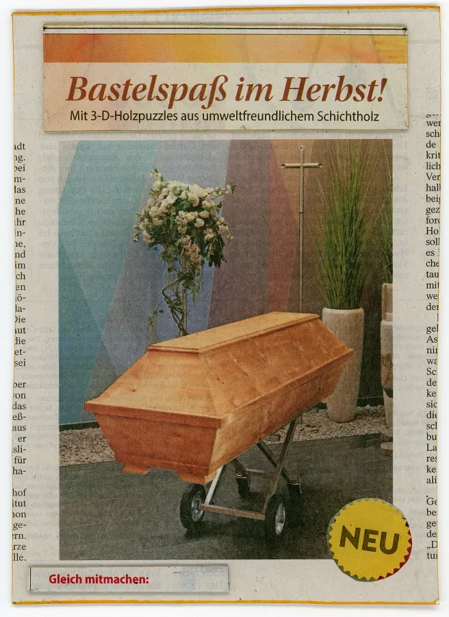 Zeitungscollage einer selbstgebauten Postkarte mit Holzsarg auf Rädern vor bunt gemusterter Wand und der Überschrift „Bastelspaß im Herbst“.