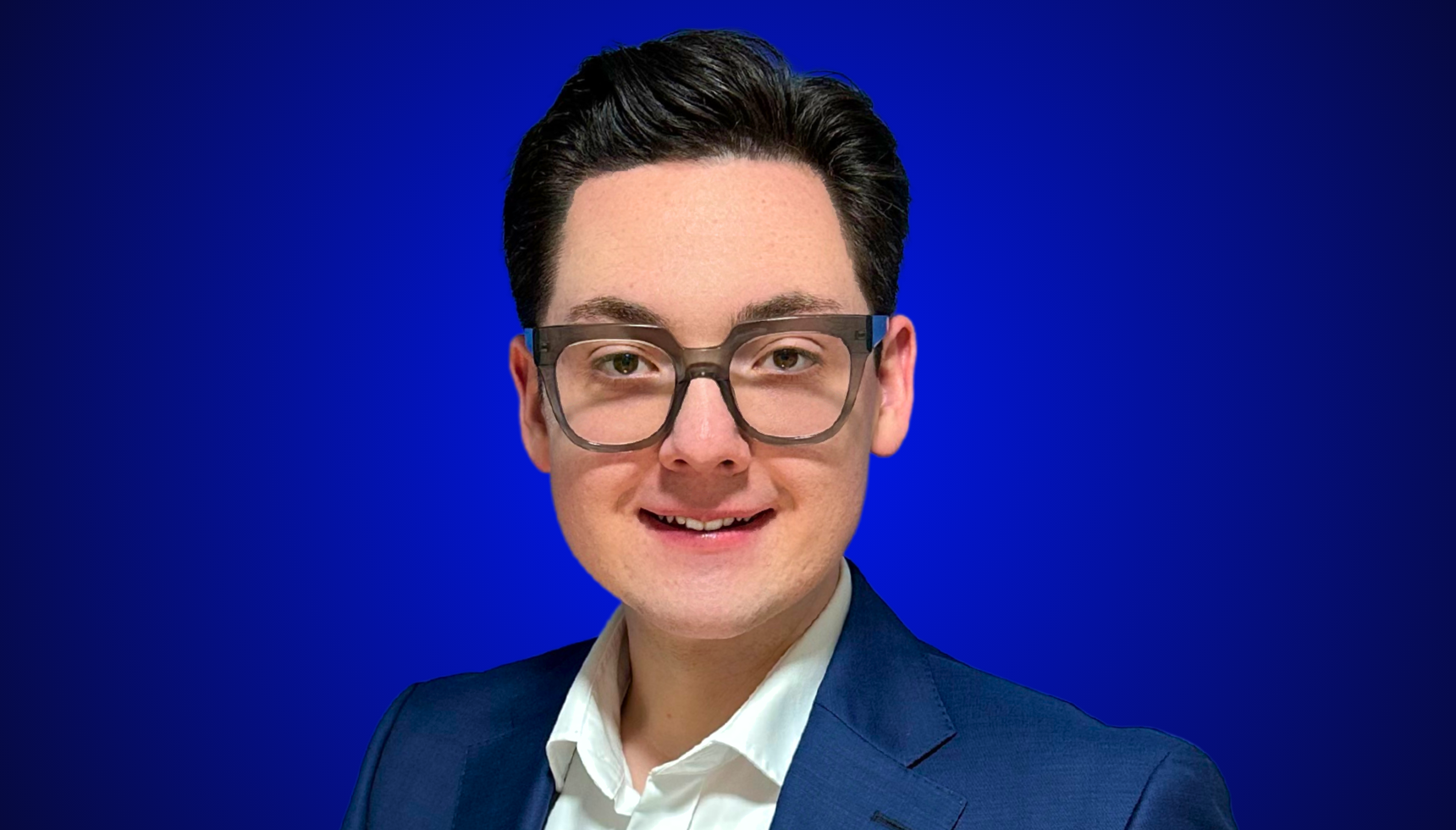 Porträt von Ricardo Dietl, Präsident der Bundesverbraucherhilfe e.V., mit weißem Hemd, dunklem Sakko und markanter Brille vor einem blauen Hintergrund.